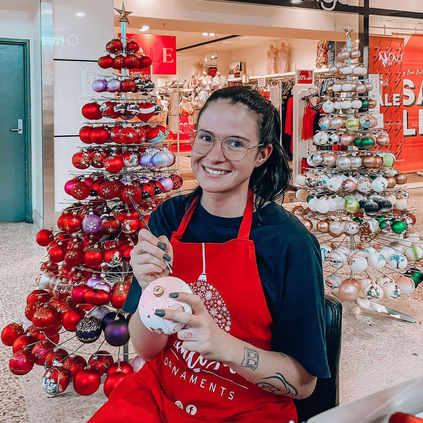 woman hand painting a christmas bauble ornament at a personalised ornament stall in a shopping centre